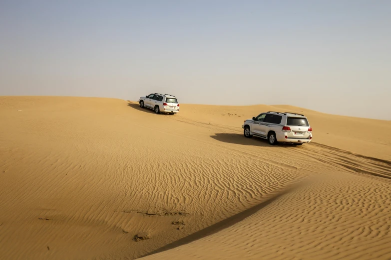 a couple of cars that are in the sand, dau-al-set, in a vast serene landscape, sand swirling, exterior shot, an intricate