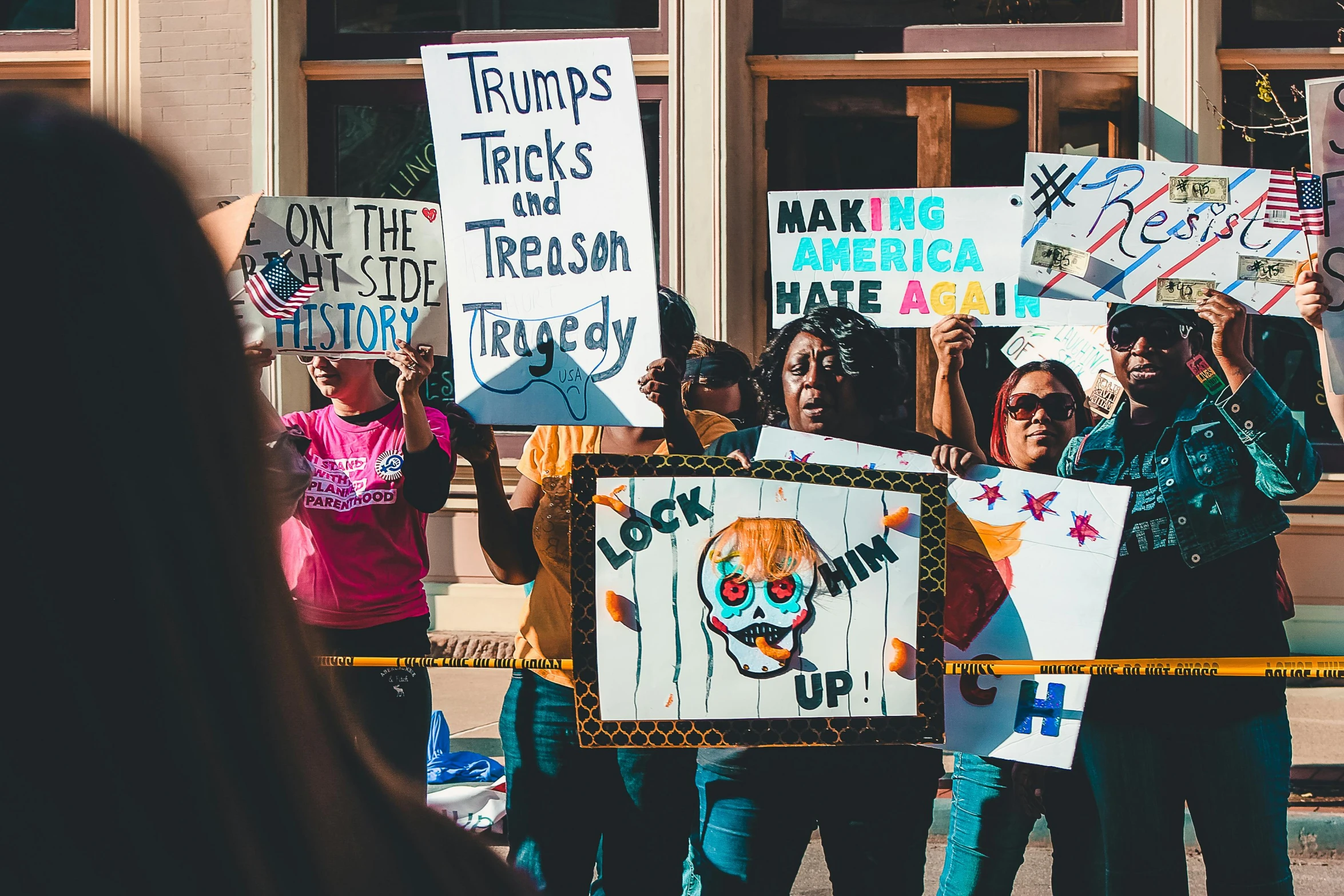 a group of people holding signs in front of a building, a photo, trending on unsplash, black arts movement, photo of donald trump, polychromatic, view from the streets, cruelty