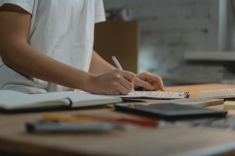 a person sitting at a desk writing on a piece of paper, pexels contest winner, cardboard, 🦑 design, background image, performance