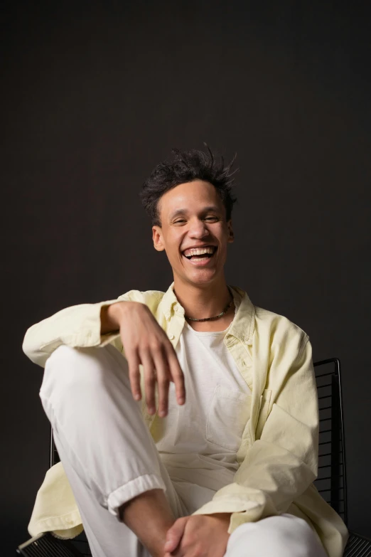 a man in a yellow shirt sitting on a chair, an album cover, trending on unsplash, brown skin man with a giant grin, nonbinary model, headshot profile picture, keith harring