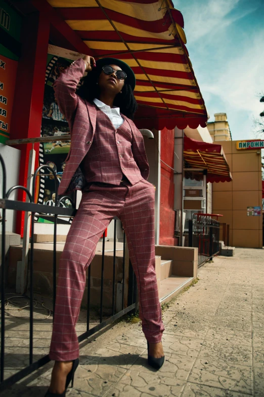 a woman in a pink suit leaning against a fence, by Carey Morris, trending on unsplash, black and red suit, standing on street corner, harlem, full body model