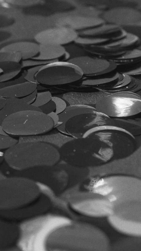a pile of coins sitting on top of a table, a black and white photo, by Attila Meszlenyi, process art, paintchips, shine, vinyl material, smooth round shapes