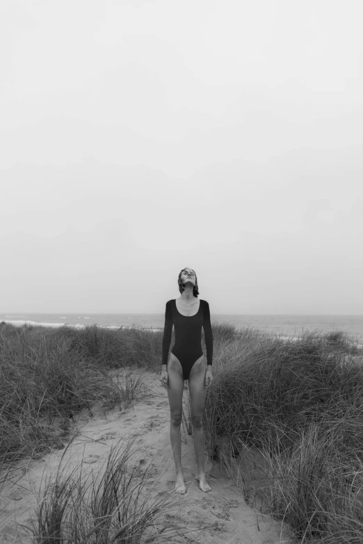 a black and white photo of a woman in a bathing suit, unsplash, conceptual art, girl walking between dunes, dreary, centered full body shot, ignant