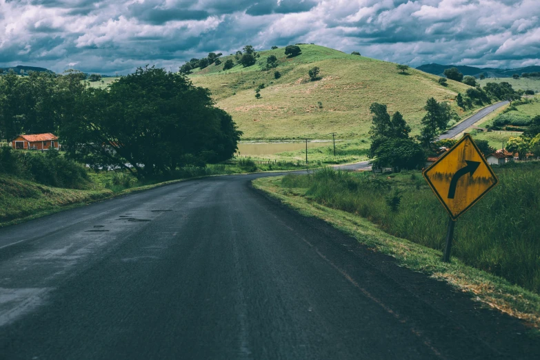 a yellow sign sitting on the side of a road, pexels contest winner, rolling green hills, wet climate, thumbnail, low light