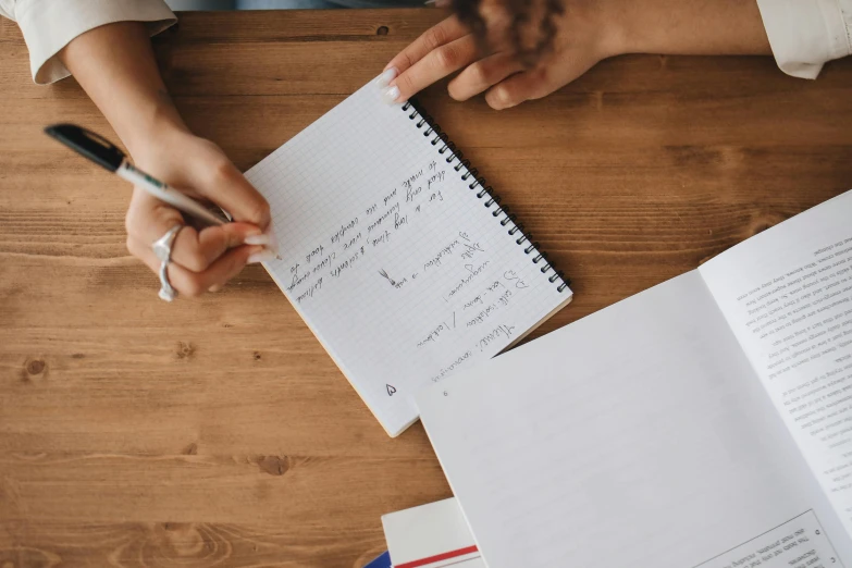 a person sitting at a table with a notebook and pen, a child's drawing, by Julia Pishtar, pexels, maths, on a wooden desk, erak note, raphael lecoste