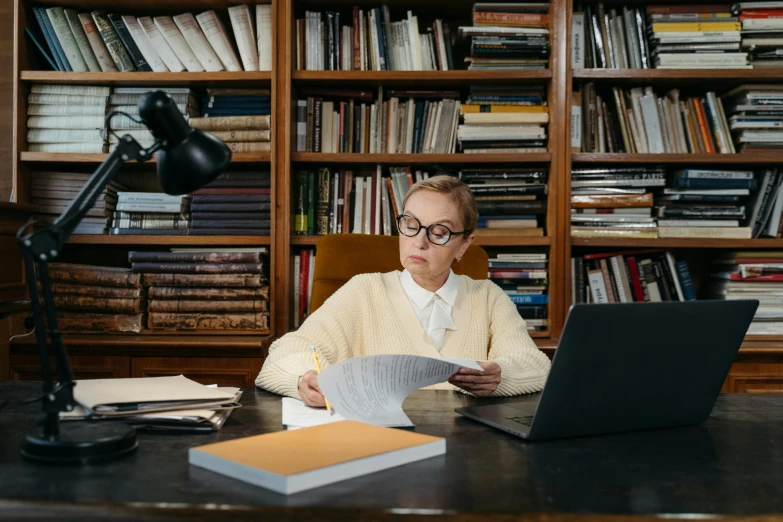 a woman sitting at a desk in front of a laptop computer, by Julia Pishtar, pexels, academic art, library nerd glasses, royal commission, professor clothes, books cave