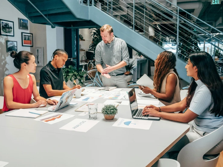 a group of people sitting around a table with laptops, by Daniel Lieske, pexels contest winner, standing on a desk, vp of marketing, carefully designed, brian ingram