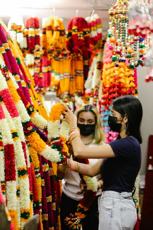 a couple of women standing next to each other in front of a bunch of flowers, hindu ornaments, facemask made of flowers, inspect in inventory image, hanging