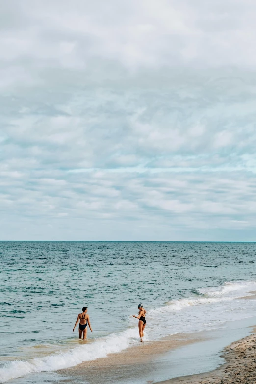 a couple of people standing on top of a sandy beach, swimming through the ocean, skies, marbella, ocean spray