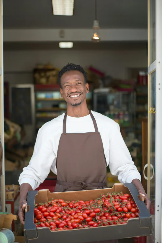 a smiling man holding a box of tomatoes, pexels contest winner, renaissance, shop front, ( ( dark skin ) ), white apron, somalia