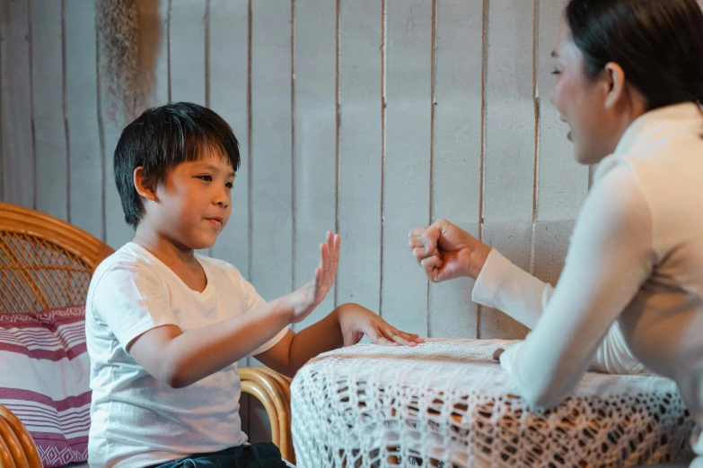 a woman and a child sitting at a table, pexels contest winner, cardistry, shrugging arms, acupuncture treatment, young boy