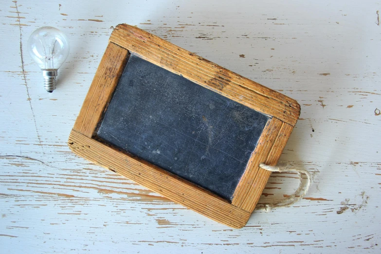 a blackboard sitting on top of a table next to a light bulb, by Jessie Algie, folk art, faded worn, carrying a tray, rectangle, shodo