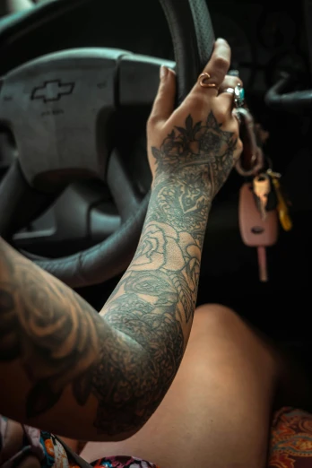 a close up of a person holding a steering wheel, a tattoo, inspired by Elsa Bleda, trending on pexels, body covered in floral tattoos, tattoo sleeve on her right arm, hands up, veins