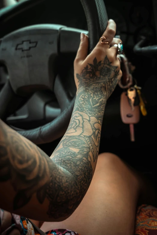 a close up of a person holding a steering wheel, a tattoo, inspired by Elsa Bleda, trending on pexels, body covered in floral tattoos, tattoo sleeve on her right arm, hands up, veins