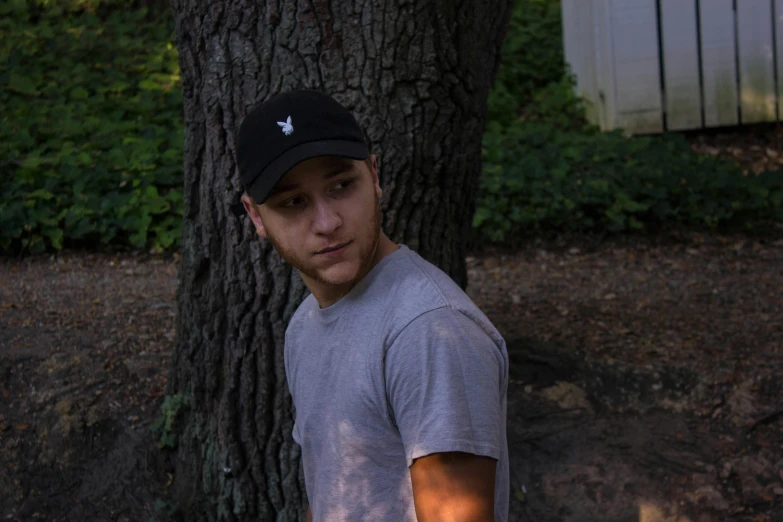 a man standing next to a tree holding a frisbee, unsplash, photorealism, wearing baseball cap, lil peep, headshot profile picture, slightly tanned