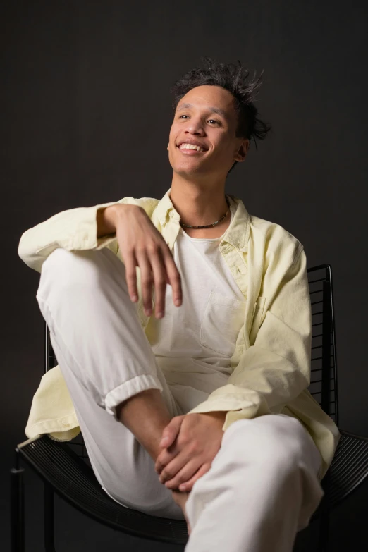 a man sitting in a chair with a smile on his face, an album cover, trending on unsplash, antipodeans, nonbinary model, white pants, portrait androgynous girl, headshot profile picture
