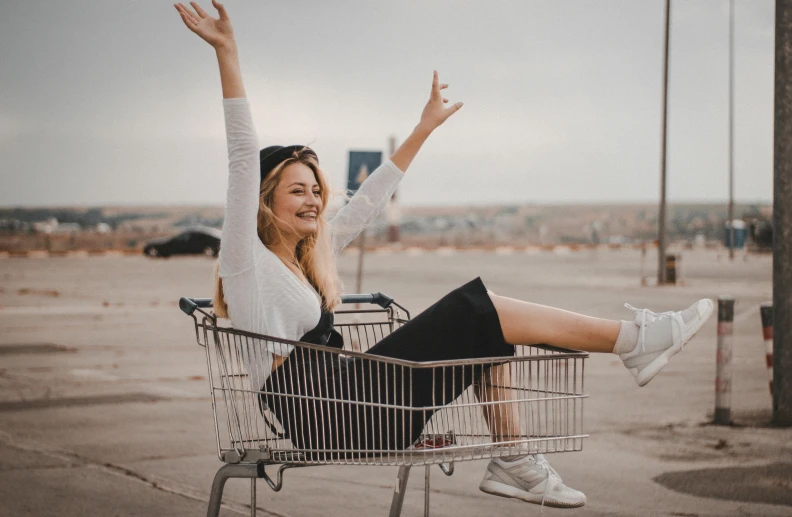 a woman sitting in a shopping cart with her arms in the air, pexels contest winner, attractive girl, wearing white sneakers, smiling girl, 2019 trending photo