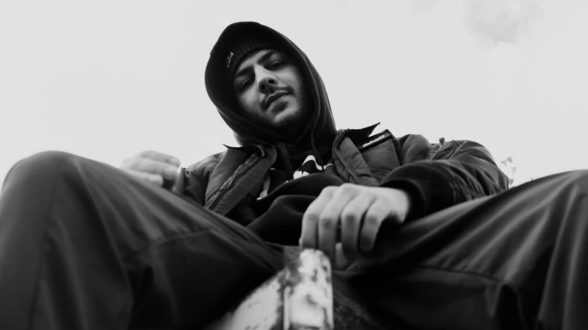 a black and white photo of a man sitting on a skateboard, wearing a hoody, sam nassour, piercing stare, wearing a tracksuit