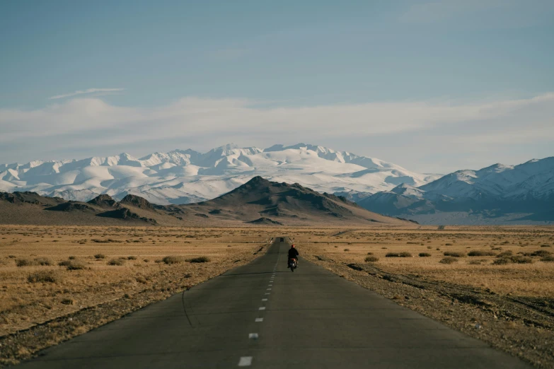 a person riding a bike down the middle of a road, by Muggur, ice mountains afar, distant photo, unsplash 4k, shot on hasselblad