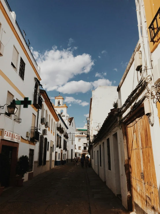 a narrow street lined with white buildings under a blue sky, a picture, trending on unsplash, seville, profile image, analog photo