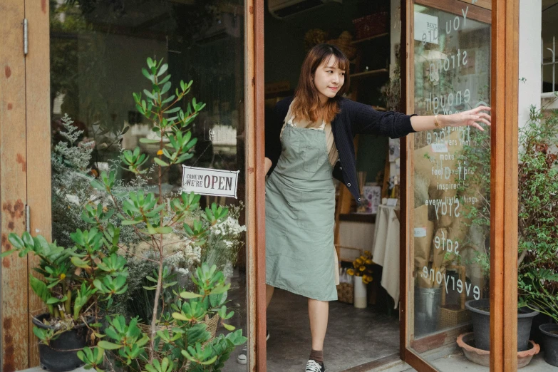 a woman standing in the doorway of a flower shop, pexels contest winner, happening, ( waitress ) girl, dark green dress, korean woman, wearing overalls