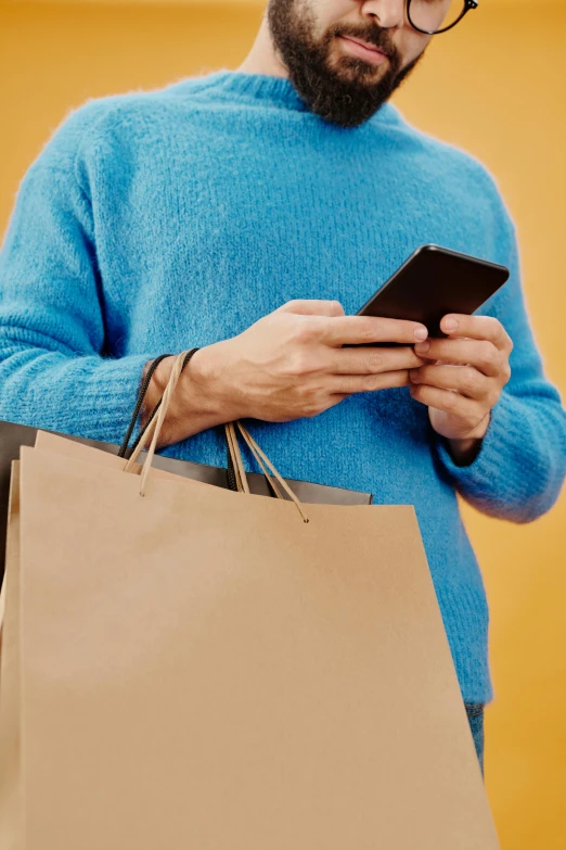 a man looking at his phone while holding a shopping bag, curated collections, square, gold, loosely cropped