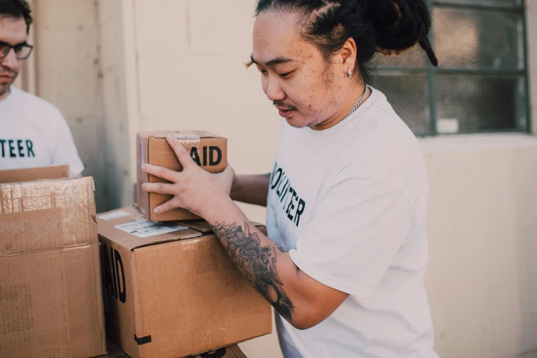 a couple of people with boxes in front of a building, profile image, tattooed, david luong, clothing drop