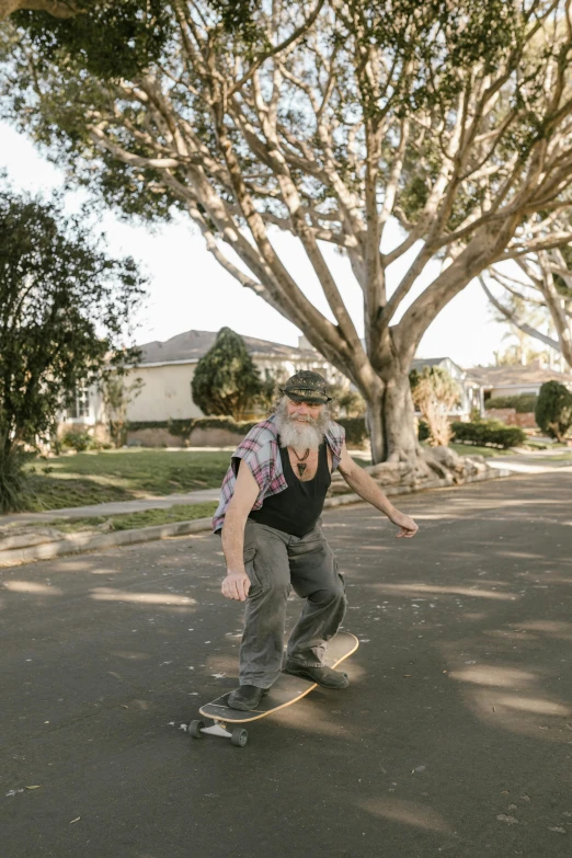 a man riding a skateboard down a street, by Winona Nelson, overalls and a white beard, neighborhood, carson ellis, 4 5 yo