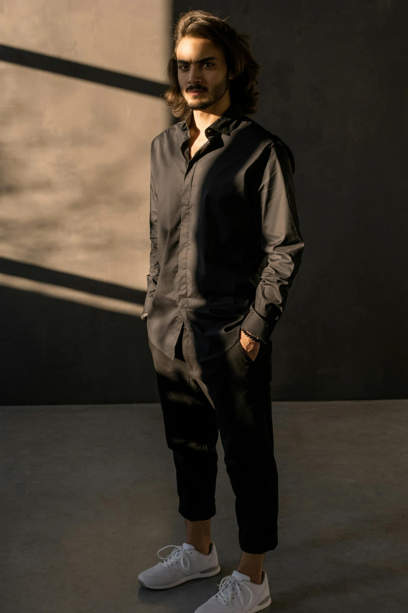 a man with long hair standing in front of a wall, jumpsuit, wearing a black shirt, style of maciej kuciara, f / 2 0