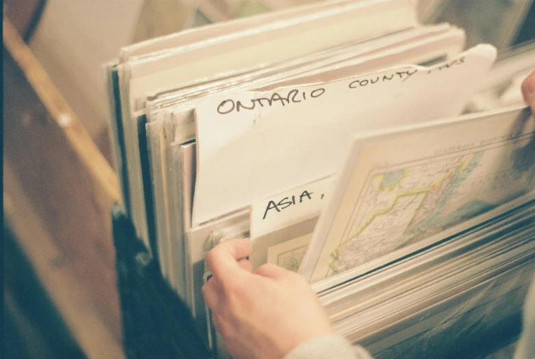 a close up of a person holding a bunch of papers, an album cover, by Matija Jama, trending on unsplash, map cartography, shelves filled with tomes, boards of canada, vintage photo