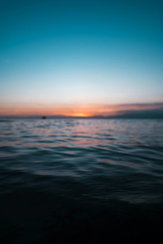 a sunset over a body of water with a boat in the distance, unsplash, minimalism, out - of - focus background, wavy water, today\'s featured photograph 4k, clear blue water