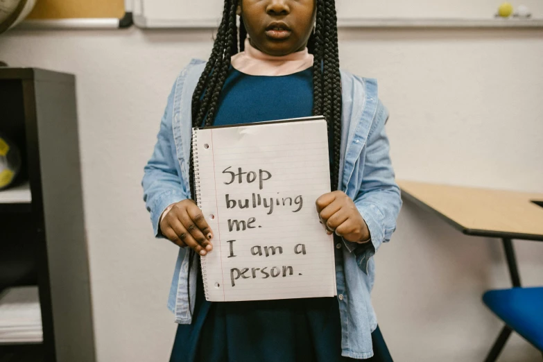a girl holding a sign that says stop bullying me i am a person, trending on pexels, afroamerican, standing in class, mundane, 1 5 0 4