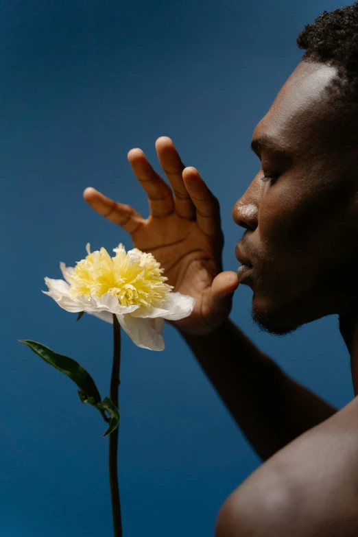 a man holding a flower in front of his face, an album cover, trending on unsplash, man is with black skin, profile image, cloudless sky, ignant