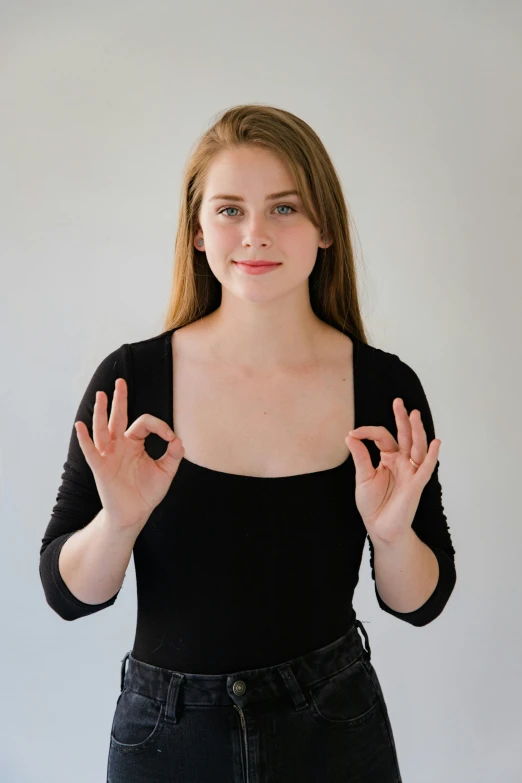 a woman making a peace sign with her hands, by Hannah Tompkins, wearing black camisole outfit, smooth pale skin, partially cupping her hands, good posture