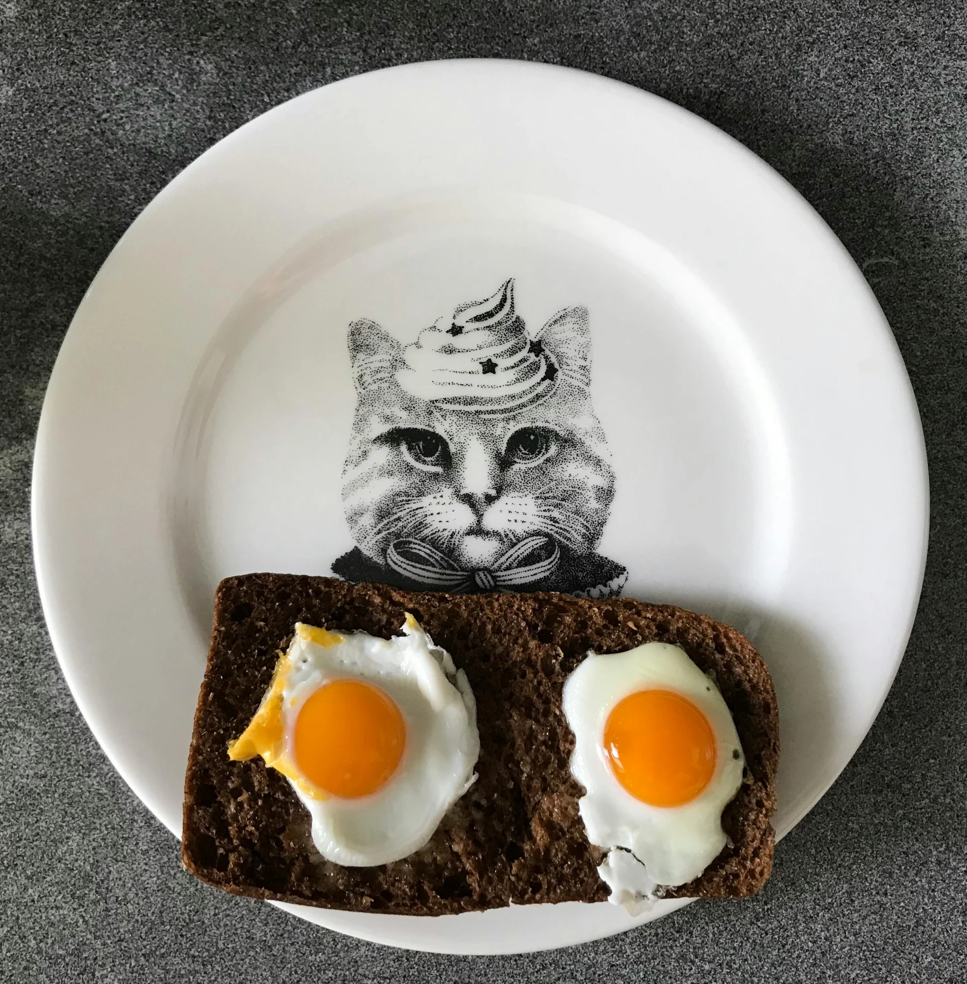 a white plate topped with two eggs on top of a piece of bread, a hyperrealistic painting, cat design, mandelbrot set, instagram picture, on kitchen table