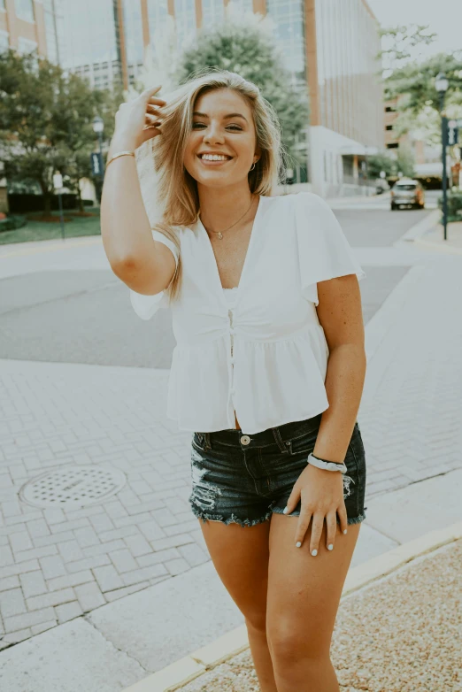 a woman standing on the side of a road, auburn outfit, wears shorts, white top, dimples
