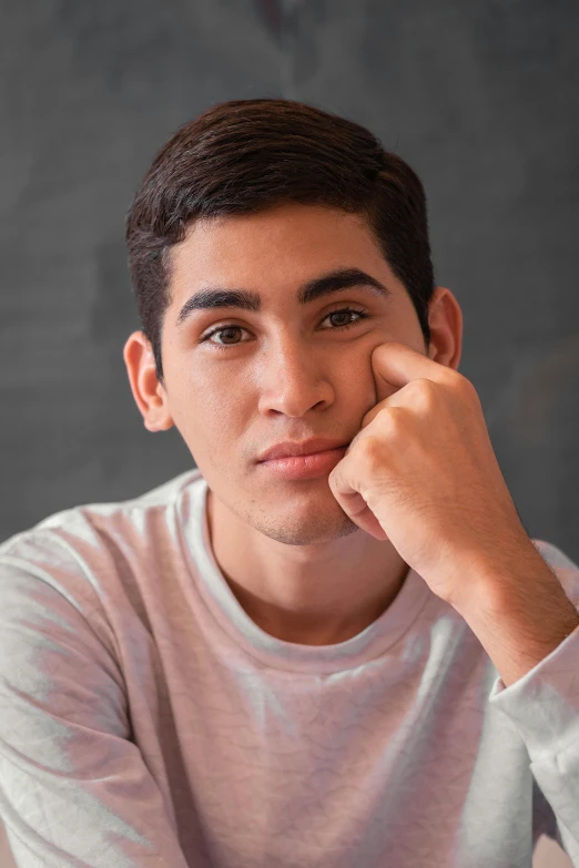 a young man sitting at a table with his hand on his chin, a picture, inspired by John Luke, trending on pexels, peruvian looking, square masculine facial features, male teenager, transgender