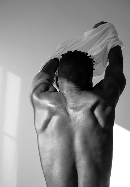 a man holding a towel over his head, a black and white photo, inspired by Robert Mapplethorpe, dark-skinned, his back is turned, morning light showing injuries, mid-shot of a hunky