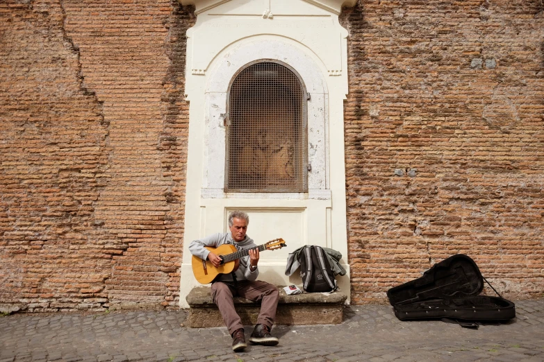 a man that is sitting down playing a guitar, an album cover, inspired by Girolamo Muziano, pexels contest winner, old city, valle dei templi, el anatsui, street vendors