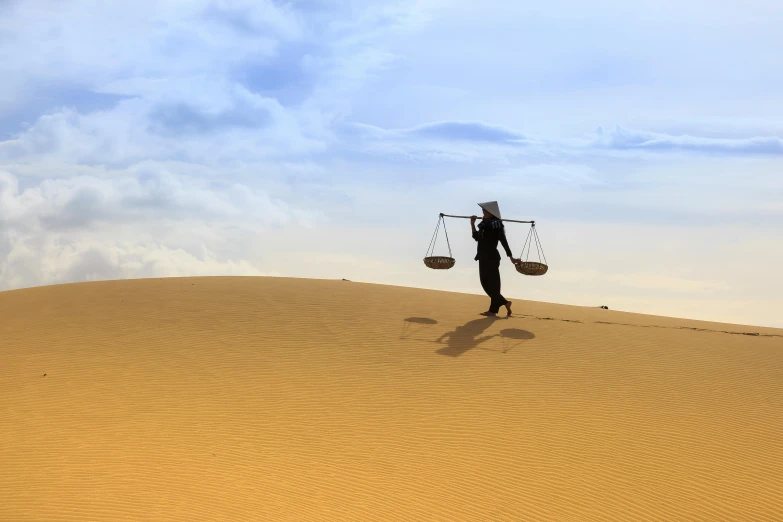 a person walking on top of a sand dune, holding scale, libra, carrying a tray, kurdish lawyer