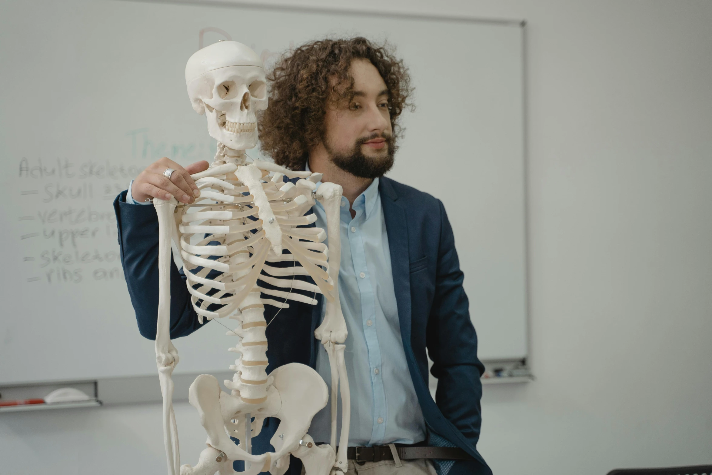 a man standing next to a skeleton in a classroom, pexels contest winner, teaching, sam hyde, human torso and head, doctor