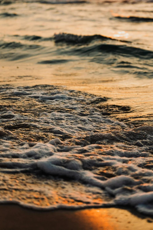 a surfboard sitting on top of a beach next to the ocean, brown water, up-close, in the evening, ocean waves