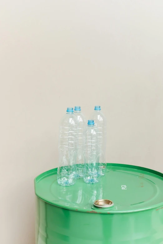 a green barrel sitting on top of a wooden floor, by Nicolette Macnamara, plasticien, water bottles, light blue water, detail shot, table