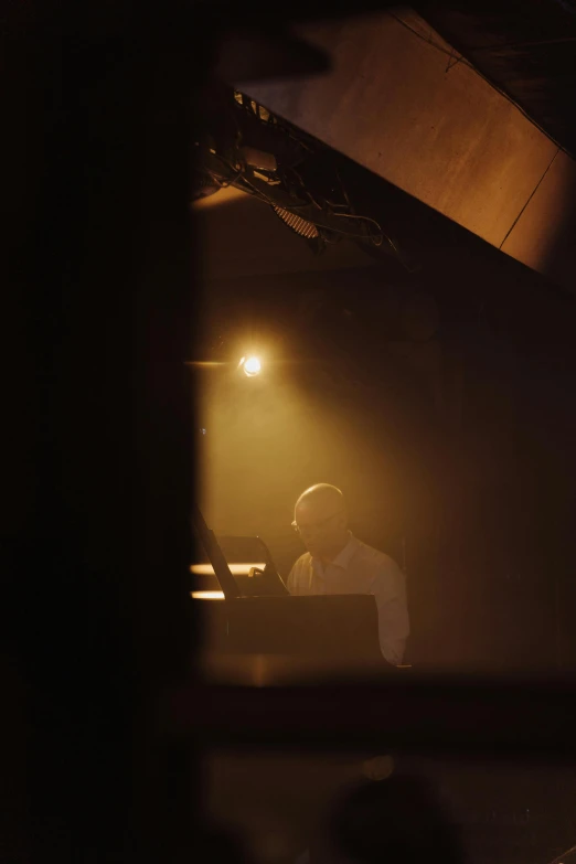 a man sitting at a piano in a dimly lit room, by Tobias Stimmer, light and space, dj set, ignant, philip selway (drums), taken at golden hour