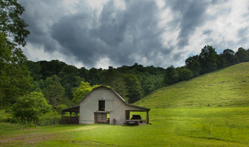 a white barn sitting on top of a lush green field, inspired by Gregory Crewdson, pexels contest winner, covered outdoor stage, gray, appalachian mountains, joel meyerowitz