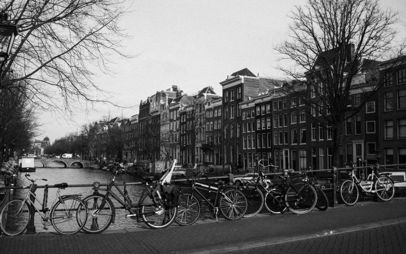a black and white photo of bicycles parked next to a canal, a black and white photo, realism, realistic »