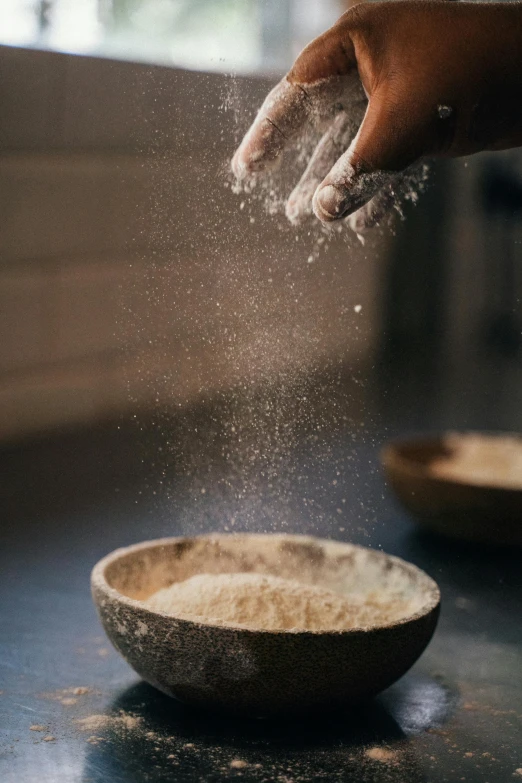 a person sprinkling flour into a bowl, a portrait, trending on pexels, natural materials, with a soft, puffy, a wooden