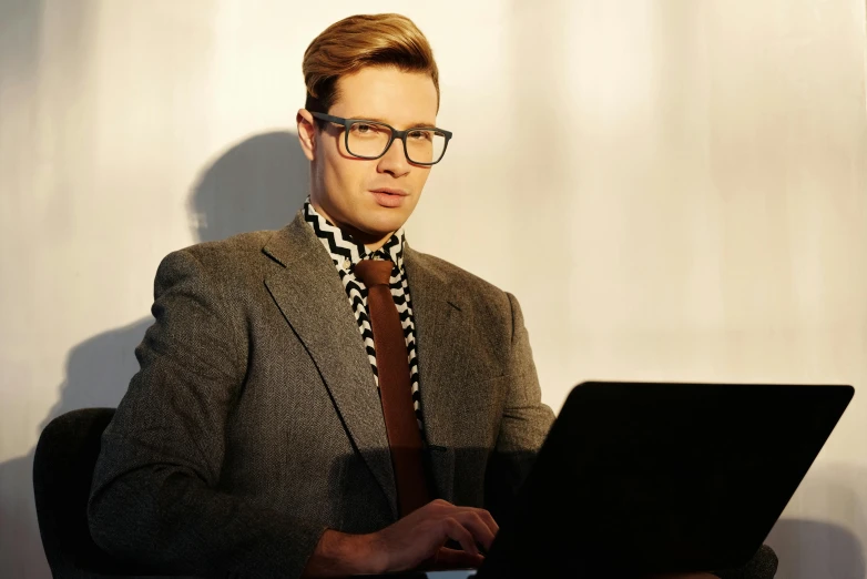 a man sitting in front of a laptop computer, an album cover, inspired by mads berg, computer art, formal attire, getty images, attractive androgynous humanoid, nerdy