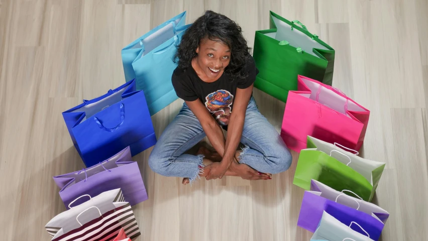 a woman sitting on the floor surrounded by shopping bags, by Bernie D’Andrea, instagram, commercial product photography, photo of a black woman, all colors, radiant smile. ultra wide shot