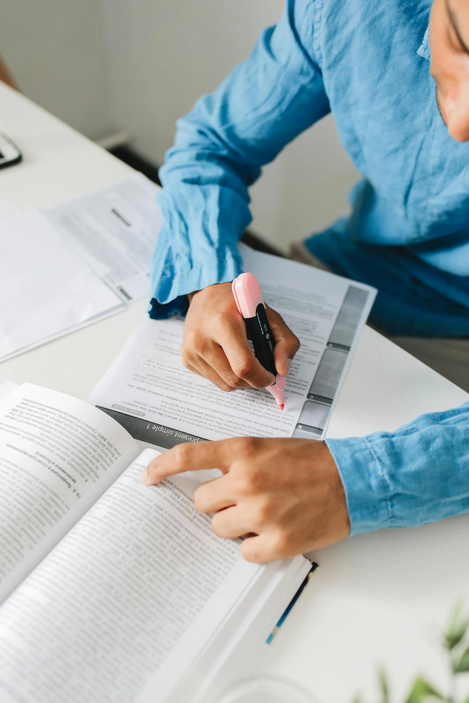 a man sitting at a table with a book and pen, wearing a light blue shirt, educational supplies, zoomed in, studious